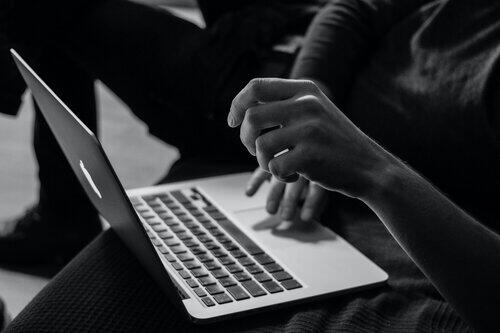 A black and white image of a person's hand using a laptop.
